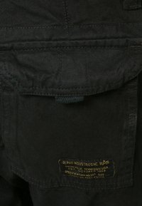 Svart arbetsjacka med en strukturerad design. Har en patchficka och en etikett med guldtext som anger märke och specifikationer.