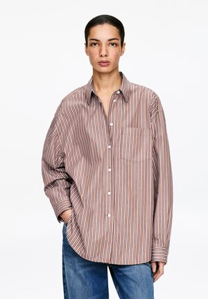 Gestreiftes Hemd mit Knöpfen in Braun und Creme, mit lockerem Schnitt, langen Ärmeln und einer einzelnen Brusttasche. Texturiertes Stoff mit sichtbaren Nähten.