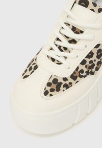 Balta sporta apavi ar gludu ādas virsu, uz kura ir leoparda raksta panelis. Apaļa purngala daļa, kurā ir šņorju aizdare, un bieza fakturēta zole.