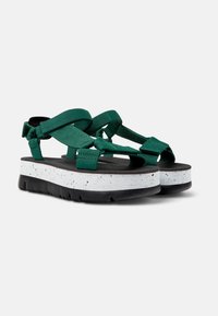 Gröna sandaler med ett tjockt vitt prickigt sula och svart mönster. Har tvärremmar och justerbara stängningar för en säker passform.