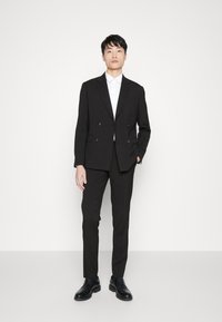 Traje negro de dos hileras con pantalones a juego, camisa de vestir blanca y zapatos de cuero negros. Textura suave y corte a medida.