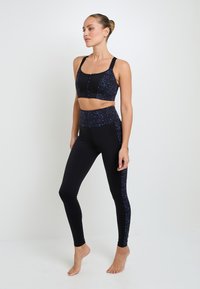Reggiseno sportivo nero e leggings con pepite multicolori. Il reggiseno ha una zip frontale; i leggings presentano pannelli laterali abbinati. Tessuto elasticizzato.