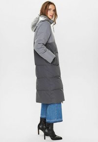 Gevoerde lange jas met grijs en zilver kleurvlakken, voorzien van een capuchon, zijzakken en een strakke textuur. Gepaard met flared denim en laarzen.
