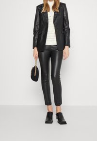 Černá kožená sako přes světle pletený krémový svetr, zkombinováno s přiléhavými černými koženými kalhotami a těžkými černými muly na podpatku.