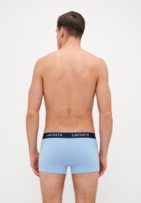 Boxers para hombre en azul claro con una banda elástica de Lacoste en navy, textura suave y diseño ajustado. Sin patrones ni acentos visibles.