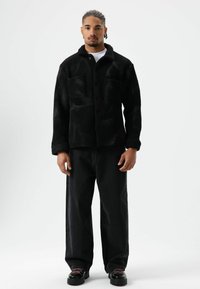 Zwart, gestructureerd jack met knopen, een kraag en twee voorzakken, gecombineerd met losse zwarte jeans en veterschoenen.