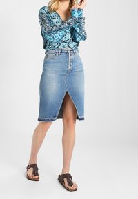 Blusa a maniche lunghe blu a fantasia, gonna a tubo in denim azzurro chiaro con spacco frontale e sandali marroni con cinturini regolabili.