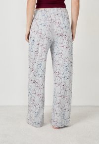 Pantalon de pyjama gris clair avec une taille élastique, présentant un motif répété d'ours en peluche aux contours bleus et maroon. Texture douce.