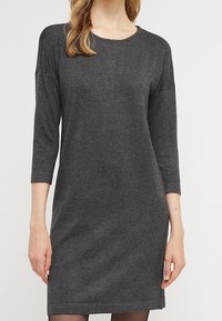 Ciemnoszara sukienka o długości trzech kwart, z okrągłym dekoltem. Charakteryzuje się prostym, prostym krojem i miękką fakturą tkaniny. Bez wzorów ani ozdób.