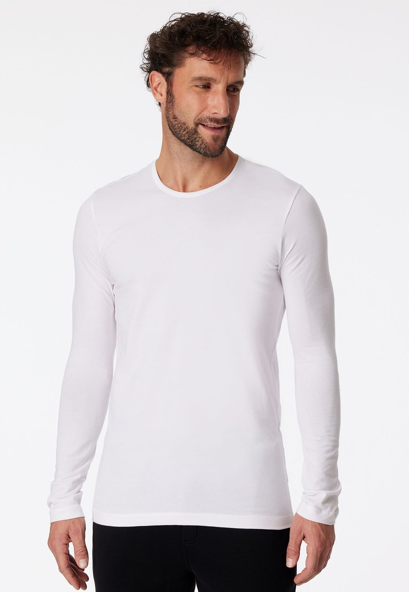 Camicia bianca a maniche lunghe con collo a giro, texture liscia e design aderente. Ideale per stratificare o per un look casual.