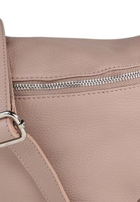 Roze leren handtas met een zilveren ritssluiting, zichtbare stiksels en een afneembare riem. De textuur is glad met een licht korrelige afwerking.