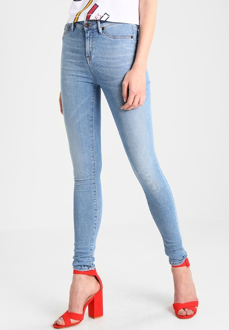 Ljusblå denim skinny jeans med en slät textur, med en midjehöjd som är måttlig och subtila blekningar, tillsammans med röda högklackade sandaler.