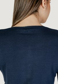 Pull en tricot bleu marine avec un col rond et un détail de marque subtil dans le haut du dos. Le tissu semble lisse et doux.