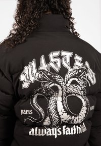 Black puffer jacket with a large silver snake graphic and stylized text on the back. Features a high collar and quilted texture.