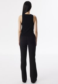 Top senza maniche nero abbinato a pantaloni neri a zampa. L'outfit presenta un design aderente e una texture liscia, evidenziando la silhouette.