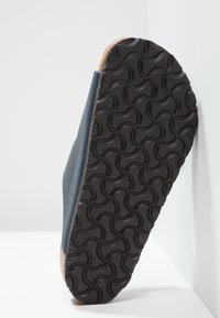 Marineblå sandaler med en teksturert svart gummisåle og korkfotseng. Har glatt overflatedesign og avrundede kanter.