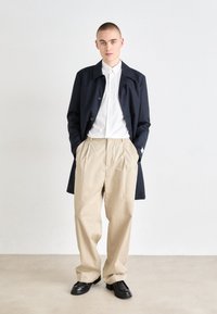 Manteau trench marine, chemise blanche à boutons, pantalon beige plissé, chaussures noires ; tissu lisse, coupe décontractée, design minimaliste, couleurs neutres.