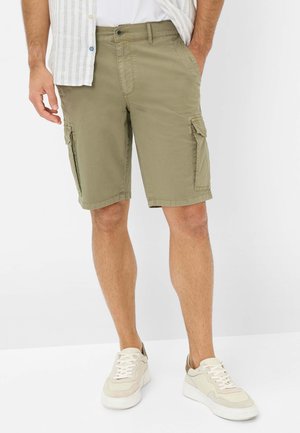 Shorts cargo vert olive avec plusieurs poches latérales, fabriqués en matériau coton léger. Associé à des chaussures de sport beige.