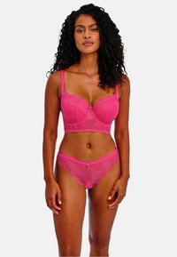 Horkorůžová krajková podprsenka a odpovídající tanga s vlnkovými okraji a mašličkovými detaily; oboje má podporu s kosticemi a jemné květinové vzory.