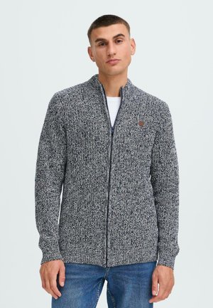 Grå og marineblå zip-up cardigan med et strukturert strikkemønster, ribbestrikkede mansjetter og et lite brunt logo-patch på venstre side.
