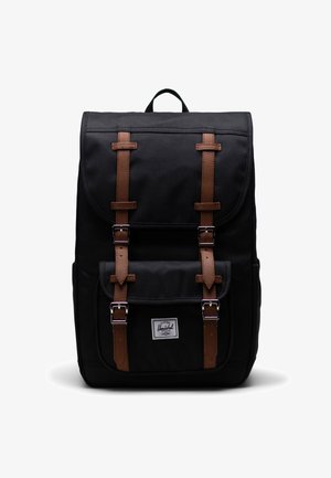 Mustapohjainen reppu, jossa on ruskeat nahkahihnat, hopeiset soljet ja etupisterekki. Varustettu yläkahvalla kantamista varten.