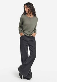 Grünes Langarmoberteil mit rundem Halsausschnitt, kombiniert mit hochgeschnittenen, weiten schwarzen Jeans aus Denim. Glatte Texturen und lässige Passform.