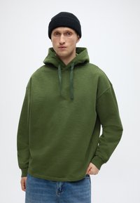 Φούτερ με κουκούλα σε ελιά πράσινο χρώμα με άνετη γραμμή, διαθέτει κουκούλα με κορδόνι και μακριά μανίκια. Συνδυάζεται με ανοιχτό μπλε τζιν, απλή υφή.