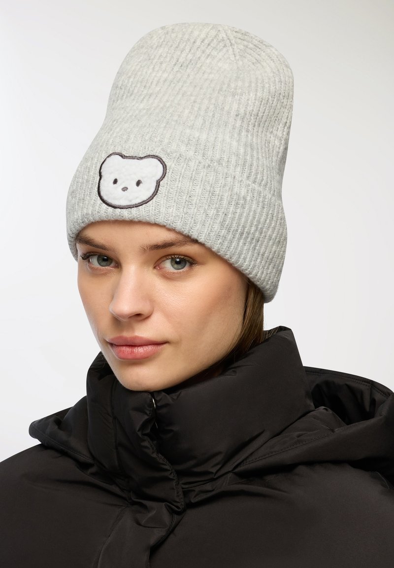 Szary sweter ściągaczowy z haftowanym na przodzie wzorem twarzy misia, w połączeniu z czarną pikowaną kurtką.