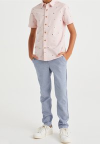 Ljusrosa kortärmad skjorta med marinblå blommönster, knappstängning fram; kombinerad med ljusblå texturerade byxor och vita sneakers.