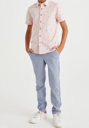 Zachtroze shirt met korte mouwen en marineblauwe bloemenpatronen, met knopen aan de voorkant; gecombineerd met lichtblauwe, gestructureerde broek en witte sneakers.