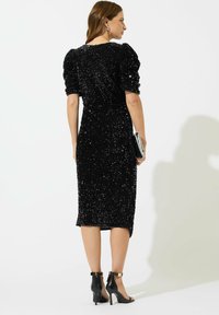 Svart paljett midi-klänning med puffärmar och en figurnära silhuett. Matchad med svarta sandaler med remmar.