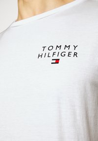 Hvit bomulls T-skjorte med svart logo med teksten "TOMMY HILFIGER" og en liten rød, hvit og blå rektangulær aksent under.