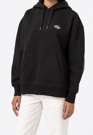 Czarna bluza z kapturem z kieszenią z przodu i małym białym logo "Dickies" na piersi, noszona z białymi spodniami.