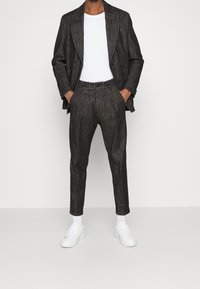 Mörkgrå skräddarsydd kostym med strukturerad tyg, enfärgad kavaj, avsmalnande byxor och vit t-shirt med rund hals. Vita sneakers fulländar looken.