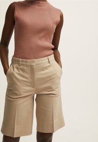 Hladký bezramenný top v jemné růžové barvě, doplněný o béžové šortky se zapracovanými kapsami a rovnými nohavicemi, s jemnou texturou.