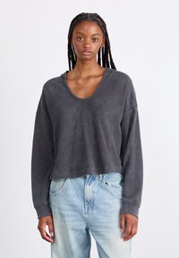 Sweatshirt court gris foncé, avec un décolleté large, des manches longues et une texture côtelée, associé à un jean bleu clair légèrement délavé.