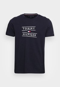 Mørkeblå bomulds t-shirt med hvid tekst "TOMMY HILFIGER" og et lille logo i rød, hvid og blå. Klassisk rund hals og korte ærmer.