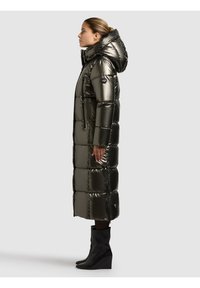 Garš tumši zaļš izolēts pūkaina mētelis ar kapuci, ar spīdīgu apdari, kabatām ar rāvējslēdzējiem un kastveida siluetu.