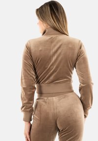 Top corto in velluto e pantaloni abbinati di un marrone chiaro, con colletto alto, polsini aderenti e una trama liscia e morbida.