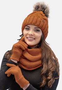 Beanie arancione lavorato a maglia con pom-pom, sciarpa abbinata e guanti. Design testurizzato con dettagli a coste, realizzato in materiale caldo e morbido.