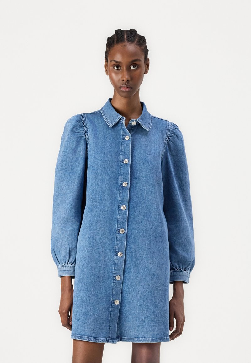 Jeansklänning med krage, knäppning fram och puffade långärmar. Tyget är ljust blått med en slät yta.