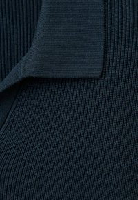 Tissu tricoté côtelé bleu foncé avec un coin plié montrant la texture et les détails de la couture serrée du matériau.