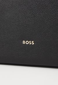 Pelle nera testurizzata con una finitura liscia, caratterizzata da un logo "BOSS" in rilievo dorato sul fronte. Leggera trama in grano su tutta la superficie.