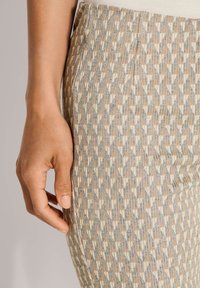 Geprint rok in beige, blauw en bruin, met een geometrisch ontwerp van textuurstof. Hand rustend op de stof nabij de taille.