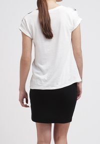 Vit kortärmad t-shirt med uppviktärmar, tillsammans med en figurnära svart minikjol. Materialet verkar mjukt och ger en avslappnad look.