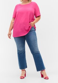 Top corto fucsia a maniche corte con scollatura rotonda, abbinato a jeans chiari a zampa d'elefante e sandali con tacco largo rosa. Tessuto con finitura liscia.