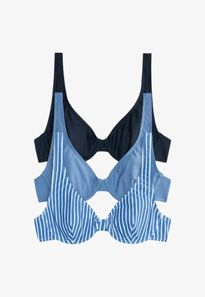 Frau trägt einen blau-weiß vertikal gestreiften Bikini mit hoch tailliertem Unterteil und steht vor einem schlichten hellen Hintergrund.