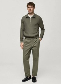 Maglione a maglia verde oliva con colletto zip, abbinato a pantaloni color olive chiaro. Mocassini neri completano l'outfit. Design semplice, texture liscia.