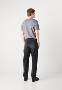 Camiseta gris de cuello redondo combinada con jeans rectos negros. Detalle destacable del logo en la cinturilla de los jeans. El modelo lleva zapatillas negras.
