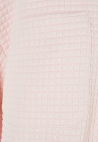 Gros plan d’un tissu rose clair avec un petit motif matelassé carré et une poche rectangulaire cousue.